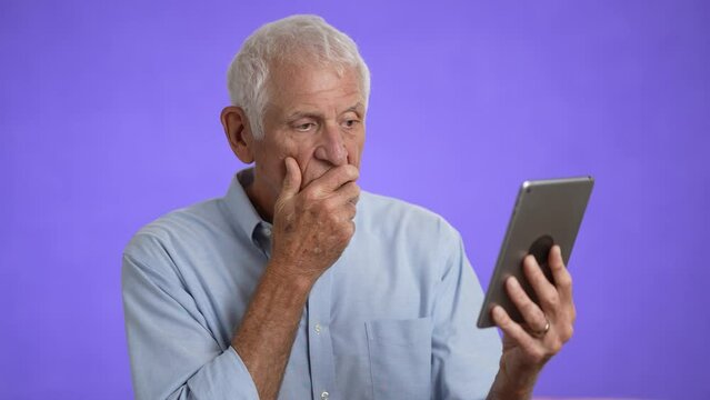 Portrait of unhappy elderly old man using tablet computer tired and getting bad news isolated on solid purple background.