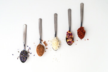 Metal spoons with different teas, spices, ingredients isolated on white. Cocoa, coconut flakes, lavender, rose petals