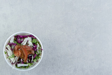 Sliced tomato, greens, red cabbage in bowl , on the marble background