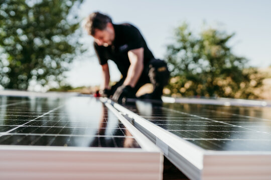 mature Technician man assembling solar panels on house roof for self consumption energy. Renewable energies and green energy concept. focus on foreground