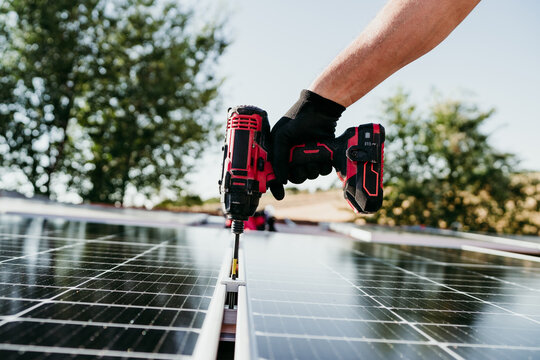close up hand of mature Technician man assembling solar panels with drill on house roof for self consumption energy. Renewable energies and green energy concept