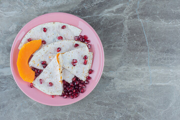 Pomegranate arils and sliced pumpkin with lavash on plate , on the marble background