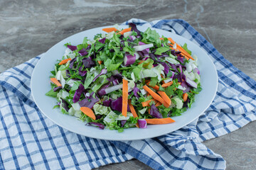 Salad prepared with fresh vegetables on plate, on the towel , on the marble background
