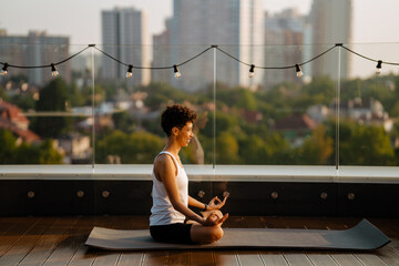 Young black woman practicing yoga on fitness mat at rooftop outdoors