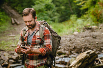 Young white man with backpack using cellphone while hiking in forest