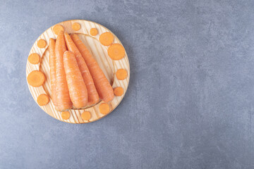 Whole and sliced carrots in the wooden plate , on the marble background