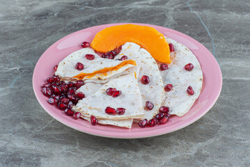 Pomegranate arils and sliced pumpkin with lavash on plate , on the marble background
