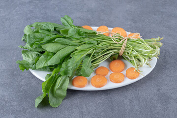 Sliced carrots with watercress on a plate , on the marble background
