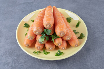 Whole and sliced carrots in the wooden plate , on the marble background