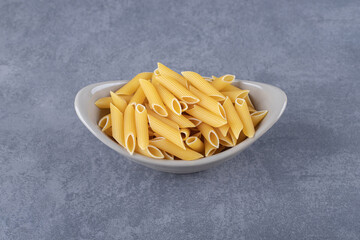 Raw penne pasta in ceramic bowl