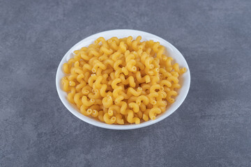 Raw elbow macaroni on white plate