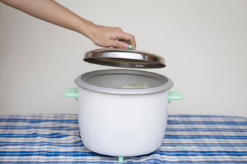 Hand opens lid of electric rice cooker after finish cooking for meal in the kitchen. Concept :...