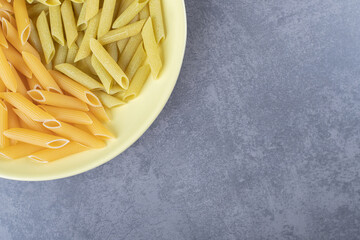 Raw green and yellow penne pasta on yellow plate