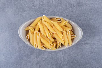 Raw penne pasta in ceramic bowl
