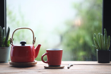Red coffee cup and red pot on wooden table in front of window