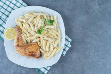 Grilled chicken leg and penne pasta on white plate