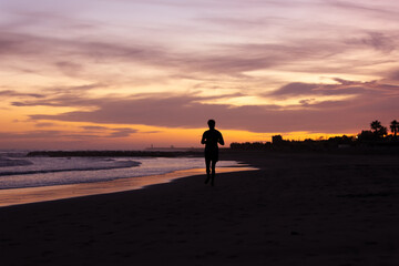 Fototapeta na wymiar Silhouette of young fitness boy of a soccer team jogging, running at sunrise beach 