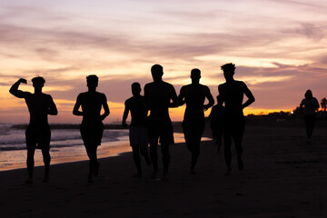 Fototapeta na wymiar Silhouette of young fitness boy of a soccer team jogging, running at sunrise beach 