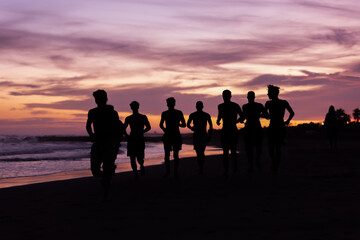 Silhouette of young fitness boy of a soccer team jogging, running at sunrise beach 