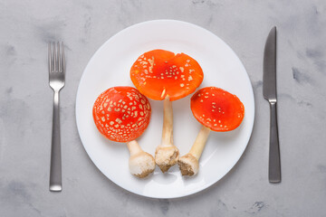 Amanita muscaria fly agaric poisonous mushrooms on plate with fork and knife top view. Consumption of hallucinogenic mushroom concept