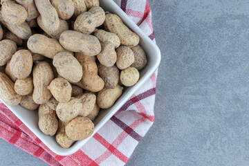 shelled peanuts in the bowl, on the towel, on the marble background