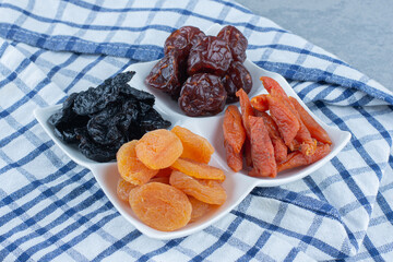 Dried cherry, apricot, plum in the bowl, on the tea towel, on the marble background