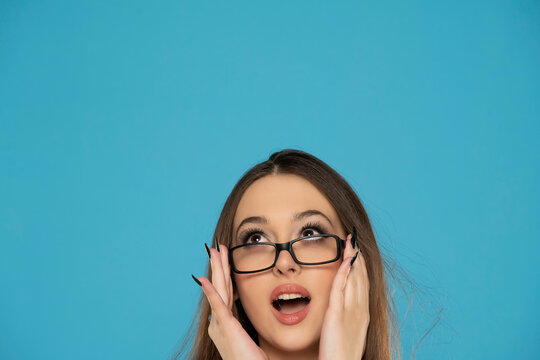 half portrait of a young surprised  woman with glasses looking up on a blue background.