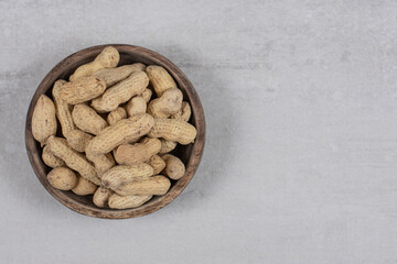 Wooden bowl of shelled peanuts on marble background