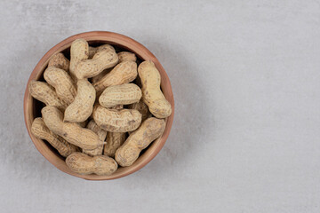 Ceramic bowl of shelled peanuts on marble background