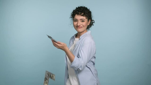 Pretty woman with happy face waste money. Young girl with blue shirt overspend US dollar currency on blue studio background