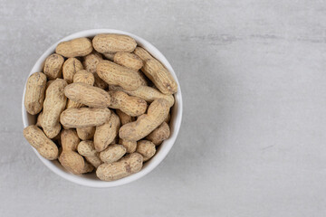 Bowl of shelled peanuts on marble background