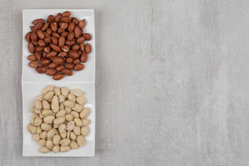 Peeled and unpeeled peanuts on white plate
