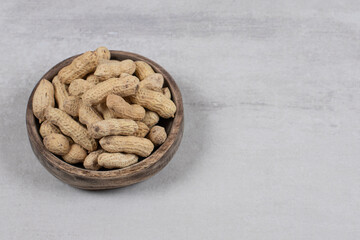 Wooden bowl of shelled peanuts on marble background
