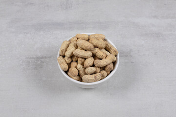 Bowl of shelled peanuts on marble background
