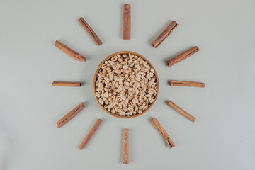 A wooden bowl full of healthy cereals with cinnamon sticks