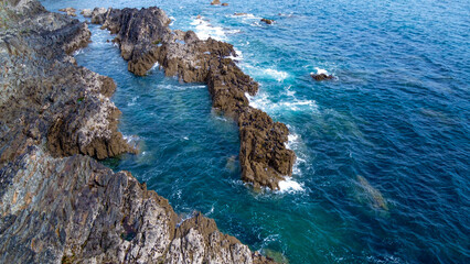 Beautiful waves break on the coastal rocks. White foam on turquoise water. Seascape on a sunny day, top view.