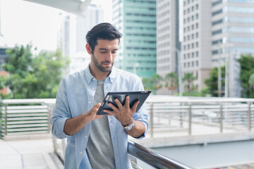 Young man using laptop computer working and video conference meeting at outdoor. Young creative man looking at screen typing message with tablet.Handsome young man using digital tablet