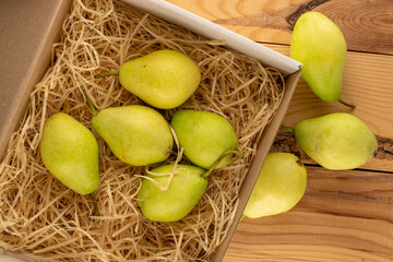 Several sweet pears in a paper box with shavings on a wooden table, macro, top view.
