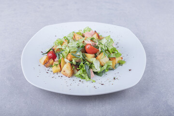 Plate of fresh salad with sausages on stone background