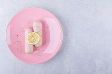 Boiled sausages decorated with lemon on pink plate
