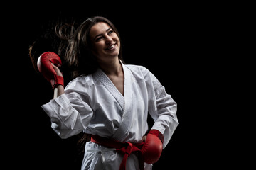 beautiful happy girl girl posing and smiling in karate outfit kimono and red gloves against black background. . © Nikola Spasenoski