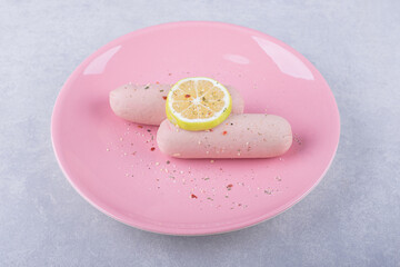 Boiled sausages decorated with lemon on pink plate
