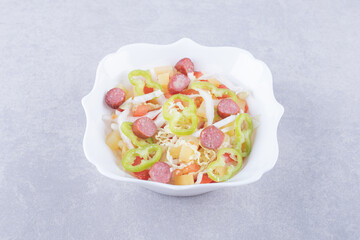 Bowl of smoked sausages and chopped vegetables on stone background
