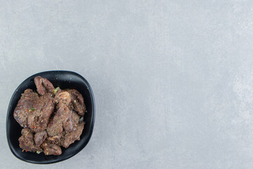 A black bowl of delicious meat on marble background