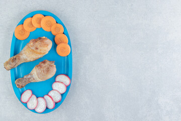 A blue wooden board of chicken fried meat and sliced radish with carrot