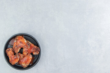 A black plate of fried meat in tomato sauce