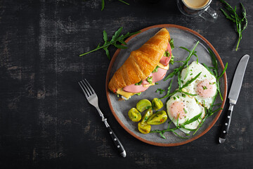 Breakfast with fried eggs and croissant sandwith with ham, cheese and salad. Delicious morning breakfast. Top view