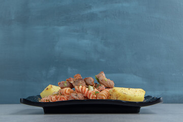 A black plate with spiral pasta with herbs
