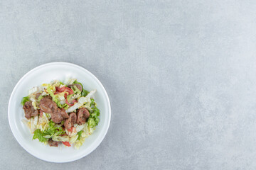A white plate of fried meat and vegetable salad