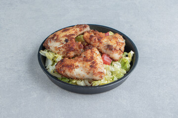 A black bowl with fried chicken legs and vegetable salad